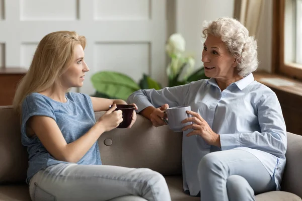 Millennial daughter drinking tea with aged mother during pleasant conversation