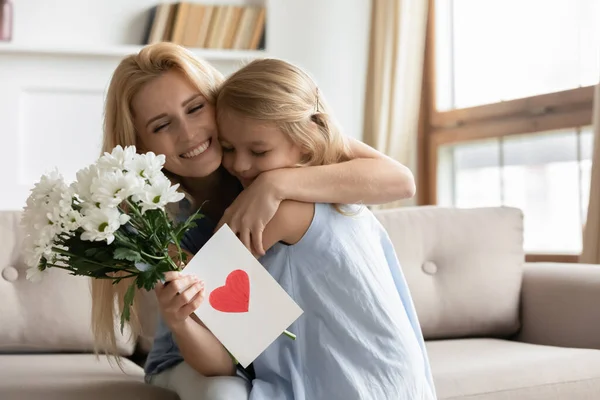 Lycklig mor kramar dotter uttrycka tacksamhet för blommor och vykort — Stockfoto