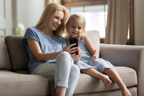 Cheerful mother showing to little daughter funny videos on smartphone — Stock Photo, Image