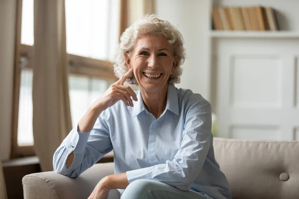 Feliz madura abuelita sentado en sofá sonriendo posando para cámara — Foto de Stock