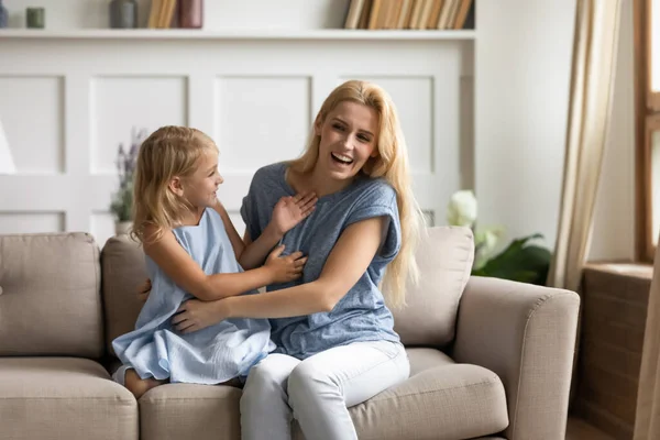 Mother play active games tickling little daughter seated on couch — Stock Photo, Image