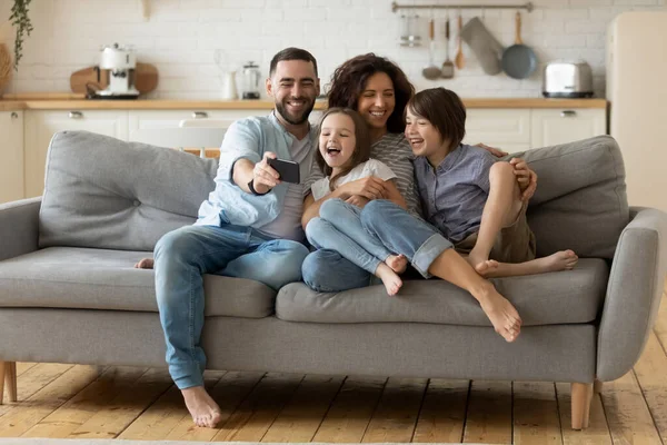 Parents souriants avec de petits enfants riant en utilisant un smartphone ensemble. — Photo