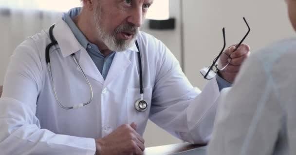 Ciddi orta yaşlı kıdemli doktor gözlüğünü çıkarıyor, hastaya danışmanlık yapıyor.. — Stok video