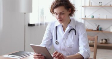 Mutlu genç bayan pratisyen doktor tablet üzerinde çalışırken eğleniyor..