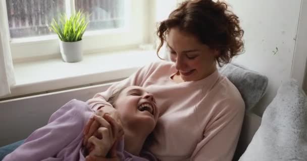 Lächelnde Frau liegt auf Couch, kuschelt lachende halbwüchsige Tochter. — Stockvideo