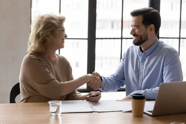 Улыбающийся менеджер пожимает руку зрелой бизнесвумен на встрече, заключает сделку — стоковое фото