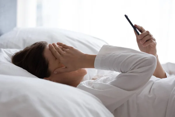 Rozrušená žena ležící v posteli četla špatné zprávy na mobilu — Stock fotografie