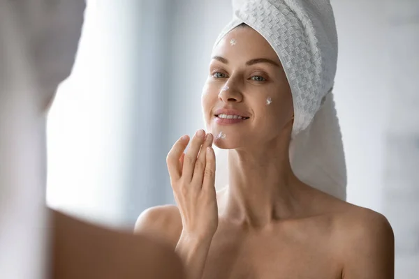 Young woman look in mirror apply moisturizing facial cream — Stock Photo, Image