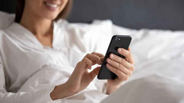 Primer plano de la mujer relajarse en la cama usando el teléfono celular — Foto de Stock