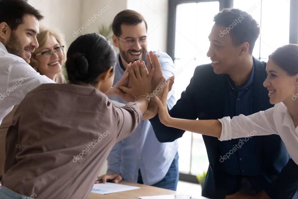 Happy diverse employees joining hands, celebrating teamwork success at meeting