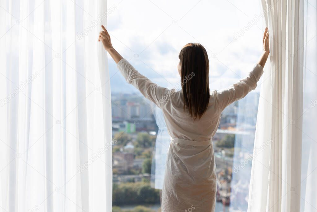 Back view of woman open curtains welcome new day