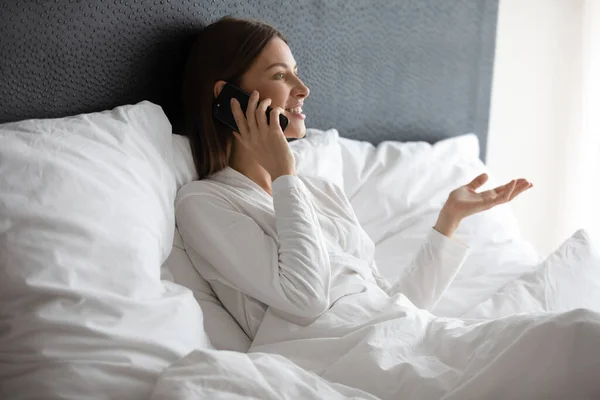 Mujer sonriente relajándose en la cama hablando en el teléfono inteligente — Foto de Stock