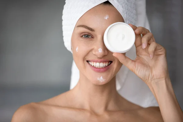 Sorridente giovane donna utilizzando crema idratante per il viso in bagno — Foto Stock