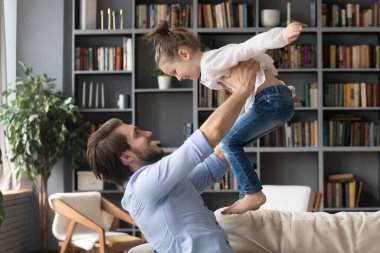 Mutlu genç baba kucağında küçük kızı uçuyormuş gibi yapıyor.