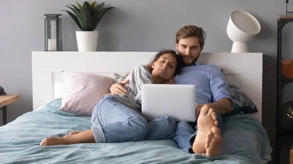 Young man and woman hugging, relaxing in bed, using laptop — Stock Photo, Image