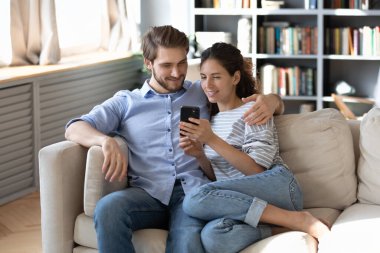 Mutlu genç çift birlikte akıllı telefon kullanıyor, kanepede dinleniyorlar.