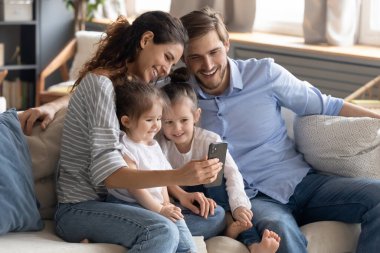 Gülümseyen genç anne ve baba ve iki kızı akıllı telefon kullanıyor.