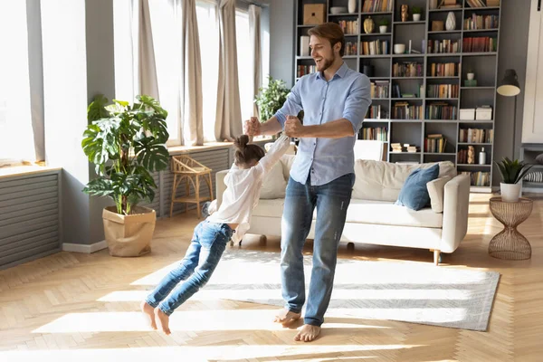 Feliz padre girando pequeña hija, jugando divertido juego en casa —  Fotos de Stock