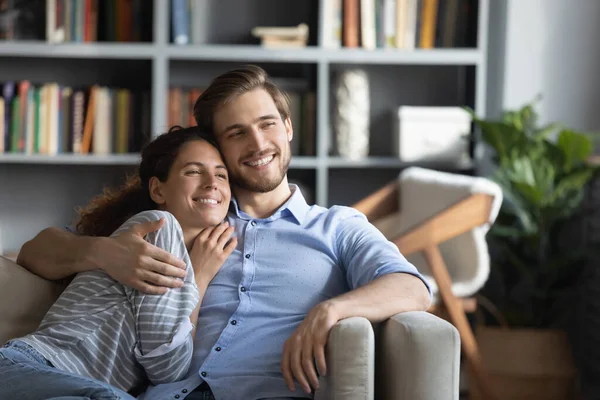 Sorrindo jovem casal sonhador abraçando, relaxando no sofá em casa — Fotografia de Stock