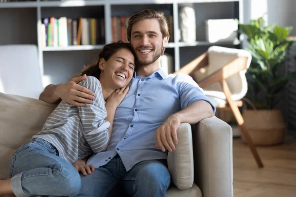 Счастливая молодая пара обнимается, смеется над шуткой, сидит на диване — стоковое фото