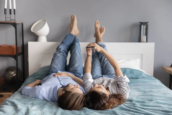 Mutlu genç çift yatakta birlikte rahatlıyor, akıllı telefon kullanıyor.