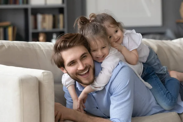Twee schattige kleine meisjes liggend op glimlachende vader terug — Stockfoto