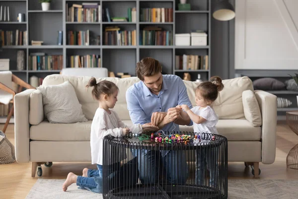 Loving father helping two little daughter making colorful beads jewelry — Stock Photo, Image