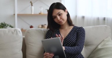 Asyalı kadın kanepede oturup arkadaşlarıyla sohbet ediyor.