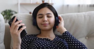 Asyalı kadınların gözleri kapalı. Kablosuz kulaklıklarla favori müziğin tadını çıkarıyorlar.