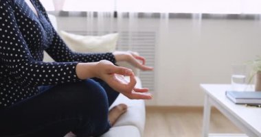 Kanepede bacak bacak bacak üstüne atmış bir kadın meditasyon yapıyor.