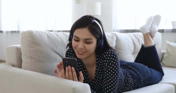 Mulher coreana usar fones de ouvido deitado no sofá usando smartphone — Vídeo de Stock