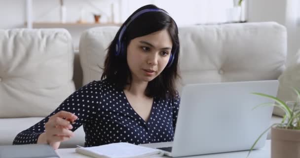 Focused asian woman studying wear headphones using pc writes notes