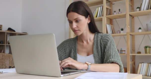 Donna d'affari concentrata che fa scartoffie lavorando sul computer portatile sedersi alla scrivania — Video Stock