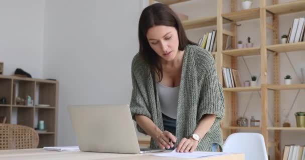 Молодая женщина-предприниматель с помощью ноутбука делает бумажную работу на рабочем месте — стоковое видео