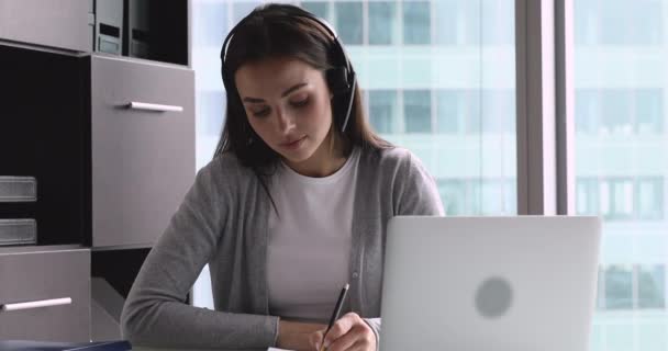 Focused businesswoman receptionist wear wireless headset video calling on laptop — Stock Video