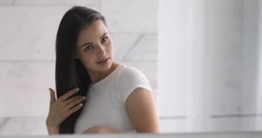 Gülümseyen, çekici, saçları tarayan, aynaya bakan genç bir kadın.