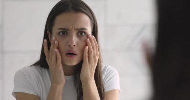 Cilt sorununa üzülmüş olarak aynaya bakan stresli genç bir kadın.