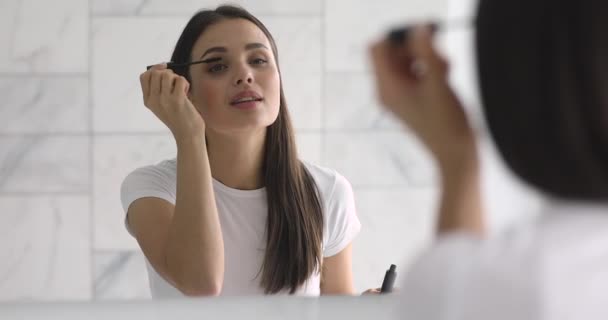 Mujer joven sonriente aplicar rímel en las pestañas mirada en el espejo — Vídeos de Stock