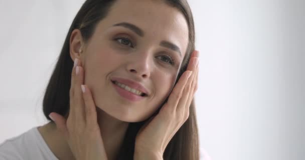 Glückliche attraktive junge Frau berührt hübsches Gesicht nach dem Auftragen von Creme — Stockvideo