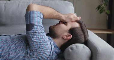Kanepede uzanmış, alnına dokunmuş bir adam migrenden muzdarip.
