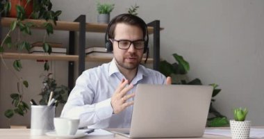Kulaklık takan adam internetten laptop ekranına bakıyor.