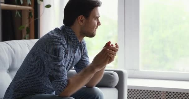 Hombre sentado en el sofá pensando mirando a la distancia se siente decepcionado — Vídeos de Stock
