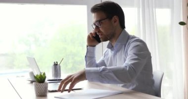 İşadamı iş yerinde oturmuş elinde akıllı bir telefonla müşteriyle konuşuyor.