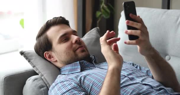 Man liggend op de bank met behulp van smartphone plezier hebben op internet — Stockvideo