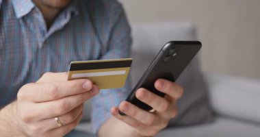 Yakın plan erkek elleri kredi kartı ve akıllı telefon tutuyor.