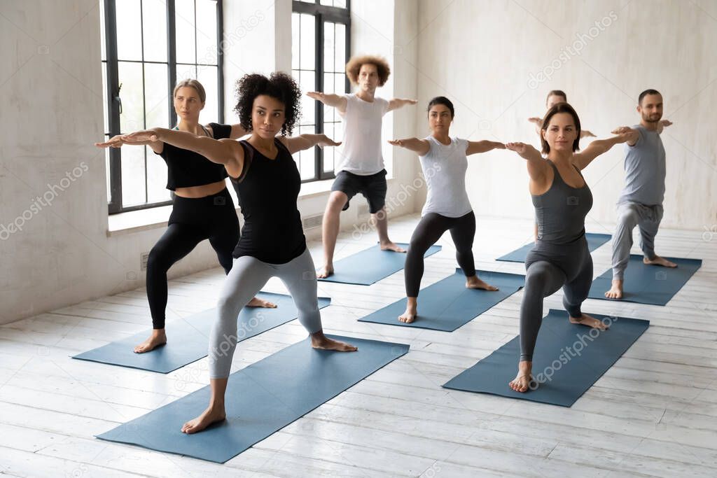 Happy mixed race people standing in warrior II pose.