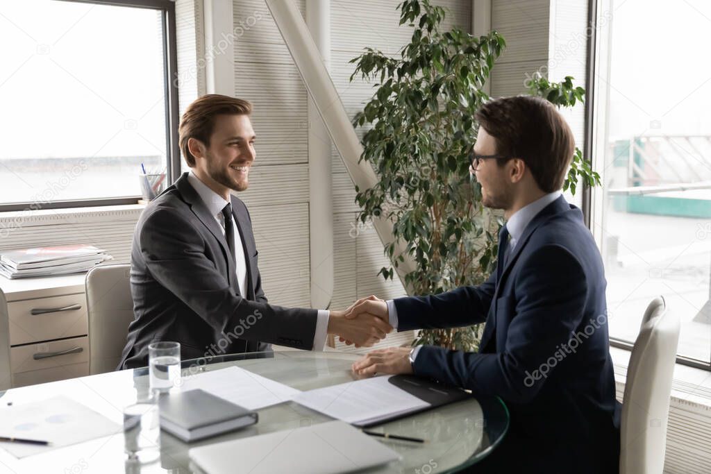 Smiling businessman handshake male employee greeting with promotion