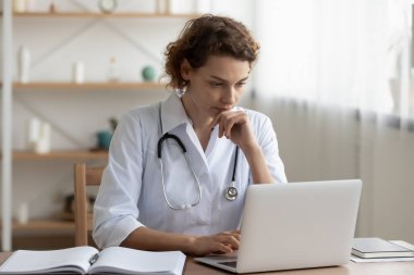 Genç bayan doktor hastanede dizüstü bilgisayarda çalışıyor.