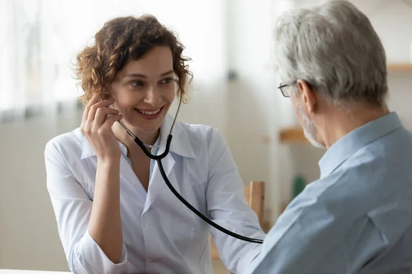 Une infirmière souriante écoute le cœur d'une patiente âgée — Photo