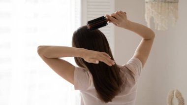 Arkadan bakan genç kadın sağlıklı, uzun düz saçları tarıyor.